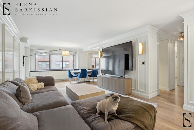 living area with decorative columns, light wood finished floors, and ornamental molding