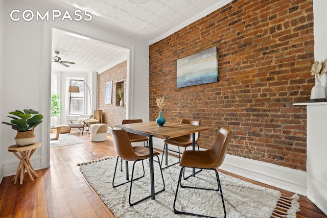 dining room with ornamental molding, a ceiling fan, hardwood / wood-style flooring, an ornate ceiling, and brick wall