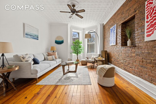 living area featuring ceiling fan, hardwood / wood-style flooring, brick wall, and ornamental molding