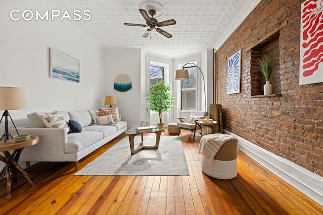 living room featuring ceiling fan, wood-type flooring, brick wall, and ornamental molding