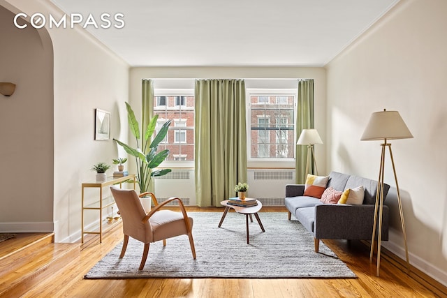 living area with arched walkways, crown molding, wood finished floors, and radiator