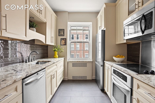 kitchen featuring light tile patterned floors, stainless steel appliances, radiator, backsplash, and a sink