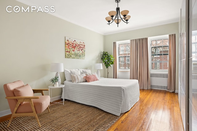 bedroom featuring baseboards, radiator heating unit, ornamental molding, light wood-type flooring, and a notable chandelier