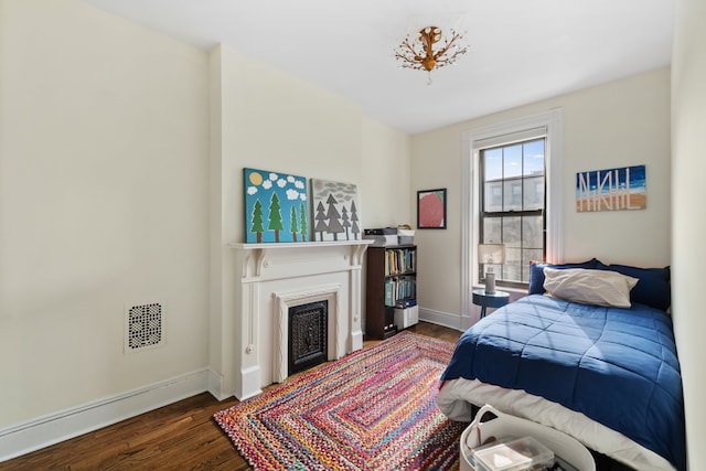 bedroom featuring visible vents, a fireplace, baseboards, and wood finished floors