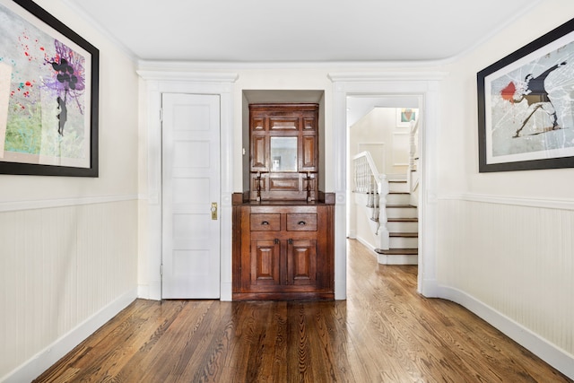 corridor with stairway, dark wood-type flooring, and wainscoting