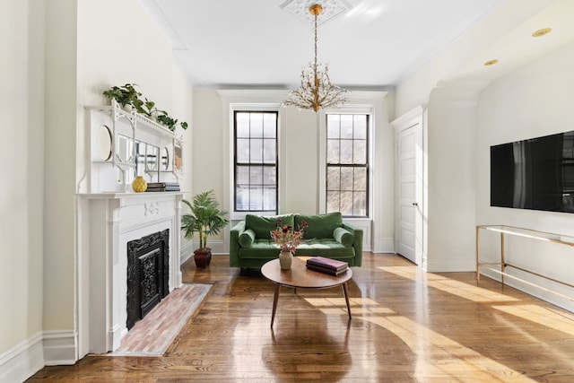 sitting room featuring a fireplace with raised hearth, baseboards, an inviting chandelier, and wood-type flooring