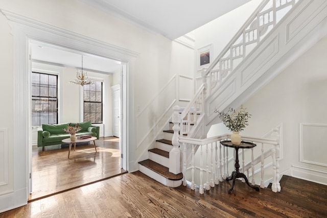 staircase with an inviting chandelier, wood finished floors, and a decorative wall