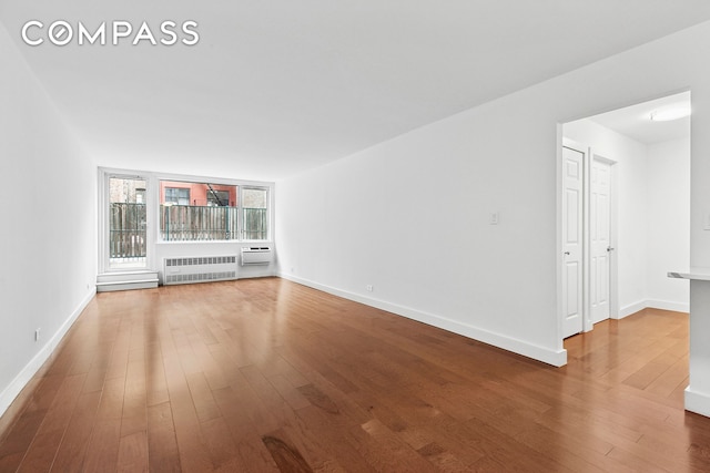 spare room featuring radiator, wood finished floors, baseboards, and a wall mounted air conditioner