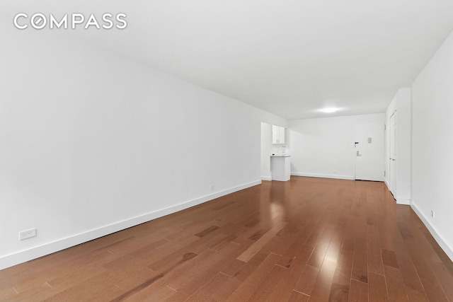 unfurnished living room featuring baseboards and dark wood-style flooring