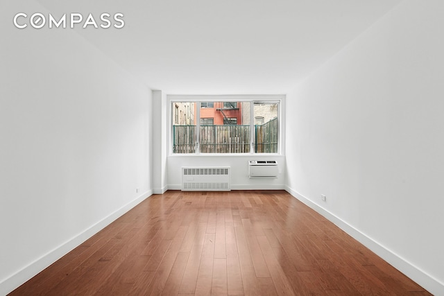 spare room featuring a wall unit AC, radiator heating unit, baseboards, and wood finished floors