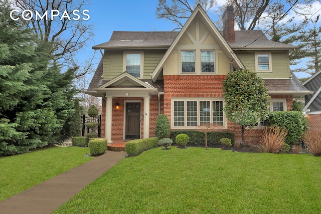 view of front of house with a front lawn, brick siding, roof with shingles, and a chimney