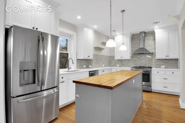kitchen featuring stainless steel appliances, wall chimney range hood, a sink, butcher block counters, and white cabinetry