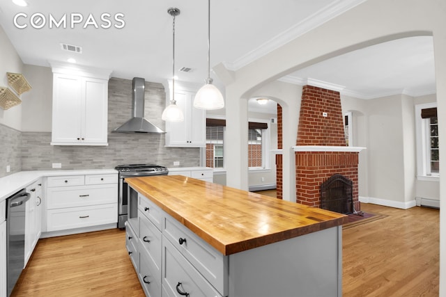 kitchen featuring white cabinetry, appliances with stainless steel finishes, a fireplace, wall chimney range hood, and wooden counters