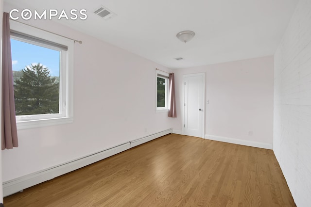 empty room with baseboards, wood finished floors, visible vents, and a baseboard radiator