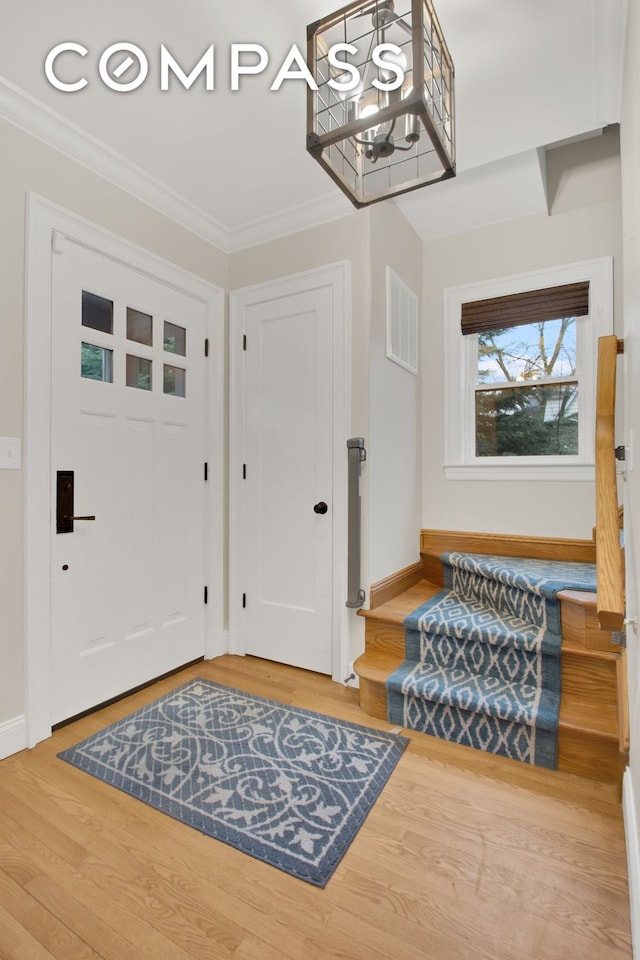 foyer with a notable chandelier, visible vents, crown molding, and light wood-style floors