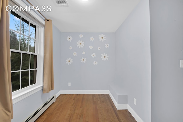 unfurnished room with a baseboard radiator, wood finished floors, visible vents, and baseboards