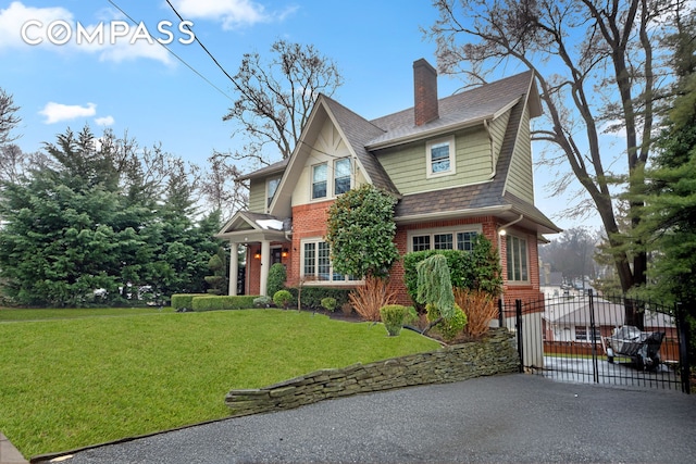 view of front of home featuring a gate, brick siding, a front lawn, and a chimney