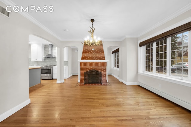 unfurnished living room featuring light wood-style flooring, crown molding, baseboard heating, a brick fireplace, and a chandelier