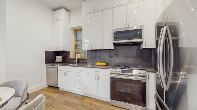 kitchen featuring light wood-style floors, appliances with stainless steel finishes, white cabinetry, dark countertops, and tasteful backsplash