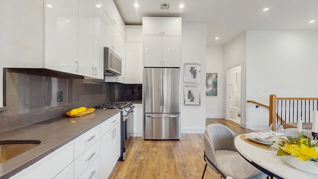 kitchen with visible vents, modern cabinets, dark countertops, white cabinetry, and appliances with stainless steel finishes