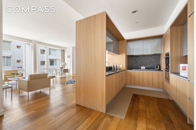 311 W Broadway Unit 5I, New York City, NY 10013 - kitchen featuring modern cabinets, a sink, backsplash, wood finished floors, and dark countertops