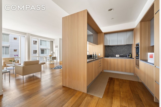 kitchen with dark countertops, light wood-style flooring, decorative backsplash, a sink, and modern cabinets