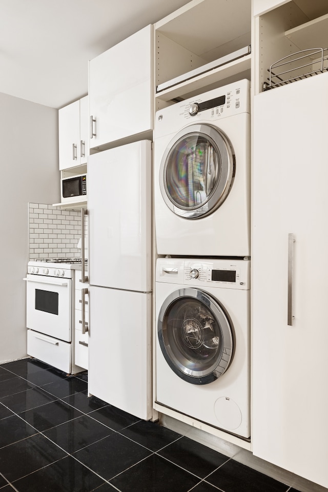 washroom with stacked washer and dryer, dark tile patterned flooring, and laundry area