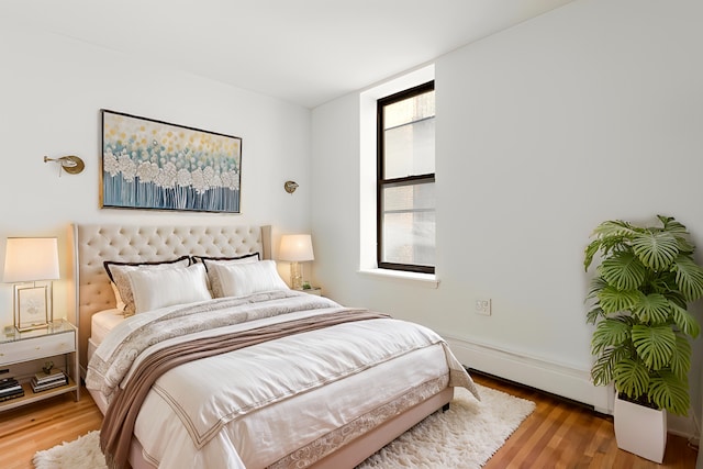 bedroom featuring multiple windows, baseboard heating, wood finished floors, and baseboards