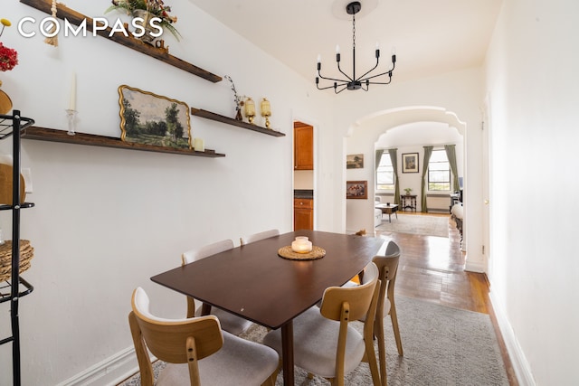 dining area featuring baseboards, arched walkways, a chandelier, and light wood finished floors