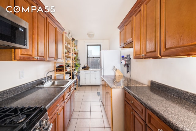 kitchen with light tile patterned flooring, freestanding refrigerator, a sink, stainless steel microwave, and brown cabinets