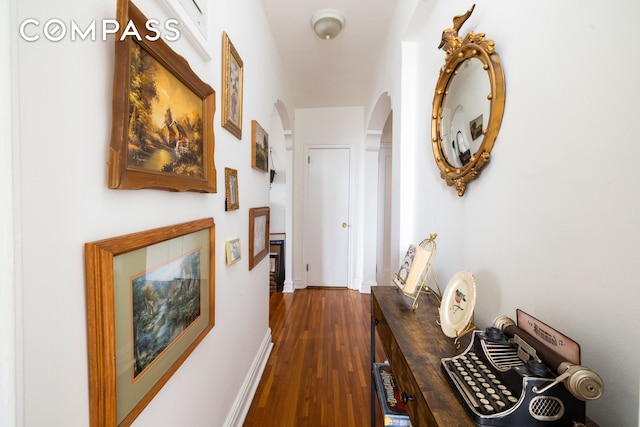 corridor with arched walkways, dark wood finished floors, and baseboards