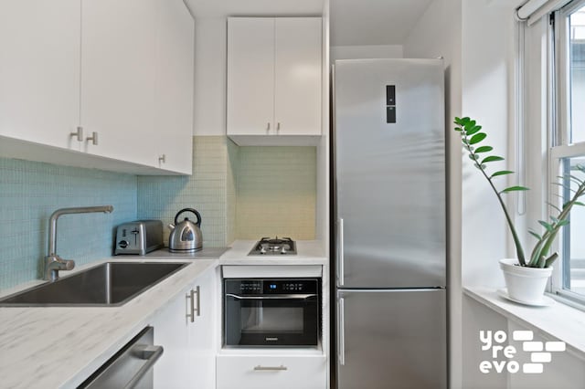 kitchen featuring appliances with stainless steel finishes, a sink, light stone countertops, white cabinetry, and backsplash