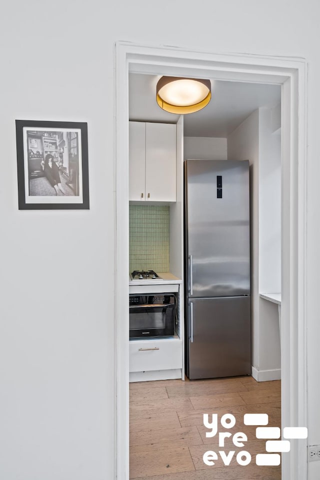 kitchen featuring wall oven, light wood-style floors, white gas cooktop, white cabinetry, and stainless steel fridge