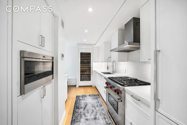 12 E 88th St Unit 6C, New York City, NY 10128 - kitchen with wall chimney range hood, stainless steel stove, wine cooler, white cabinets, and recessed lighting