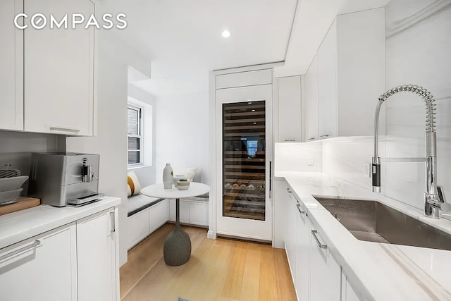 kitchen with light countertops, light wood-style flooring, white cabinetry, a sink, and beverage cooler