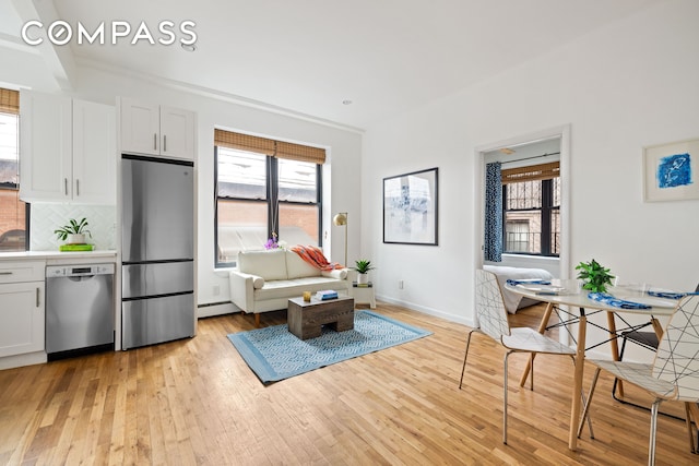 living area with light wood-type flooring, baseboards, baseboard heating, and a healthy amount of sunlight