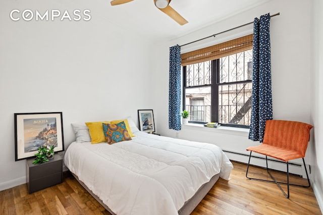 bedroom with baseboards, baseboard heating, wood finished floors, and a ceiling fan