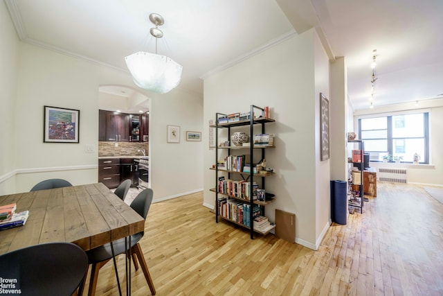 dining space featuring radiator, light wood finished floors, baseboards, and crown molding