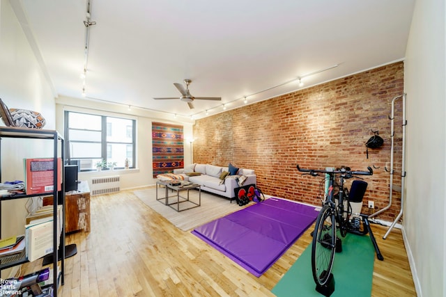 workout room with a ceiling fan, brick wall, radiator heating unit, wood finished floors, and rail lighting