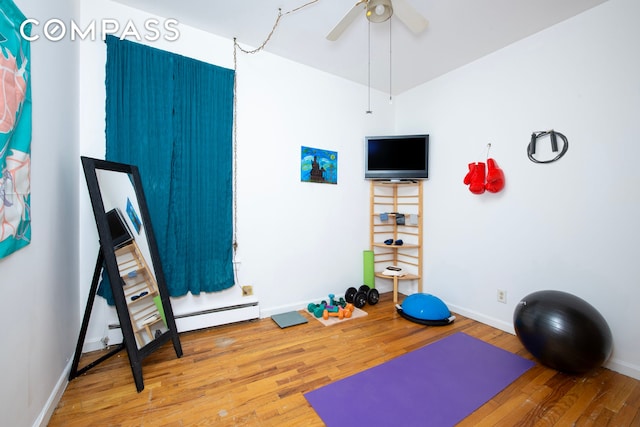 workout room featuring a ceiling fan, a baseboard radiator, baseboards, and wood finished floors