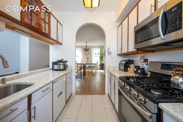 kitchen with arched walkways, stainless steel appliances, a sink, backsplash, and glass insert cabinets