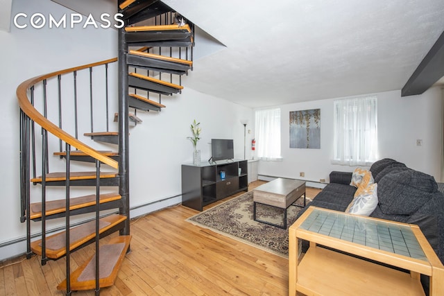 living room with a baseboard heating unit, wood-type flooring, and stairway