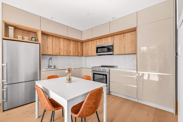 kitchen featuring appliances with stainless steel finishes, a sink, light wood-style flooring, and decorative backsplash