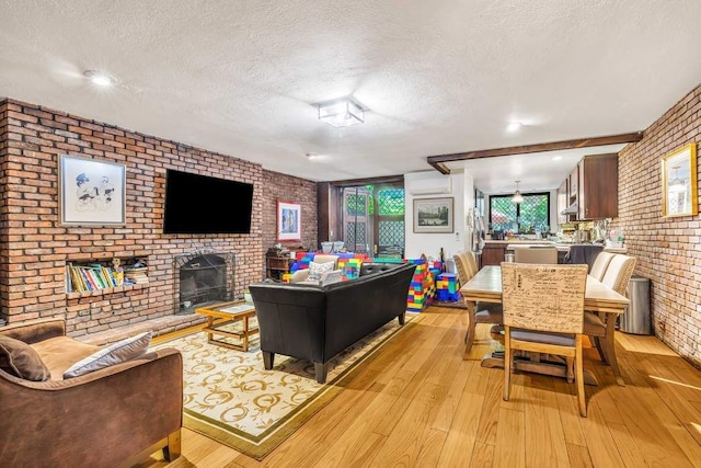 living room with light wood finished floors, brick wall, a textured ceiling, an AC wall unit, and a brick fireplace