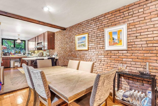 dining area with light wood-style floors, brick wall, and beam ceiling