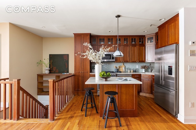 kitchen featuring light wood-style flooring, glass insert cabinets, appliances with stainless steel finishes, light countertops, and decorative backsplash