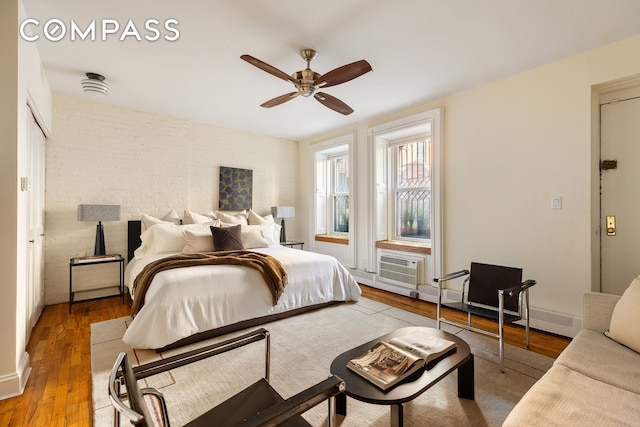 bedroom featuring a wall unit AC, ceiling fan, brick wall, and wood finished floors