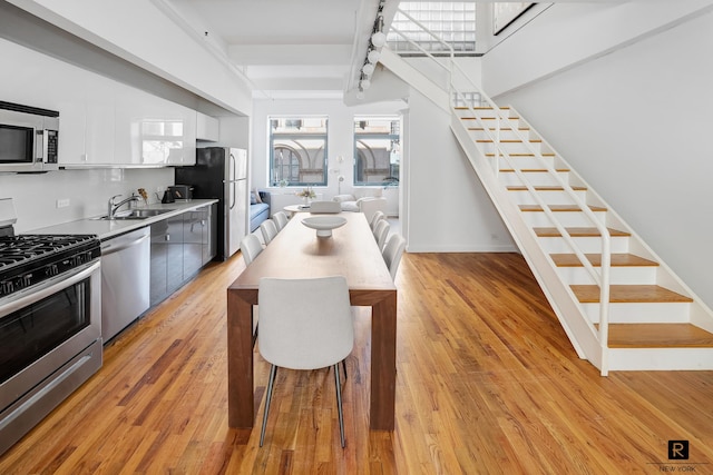 kitchen featuring white cabinets, stainless steel appliances, light countertops, light wood-type flooring, and a sink