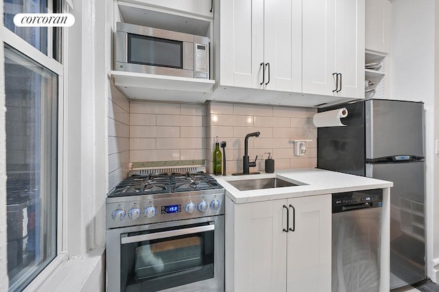 kitchen featuring appliances with stainless steel finishes, white cabinetry, a sink, and tasteful backsplash