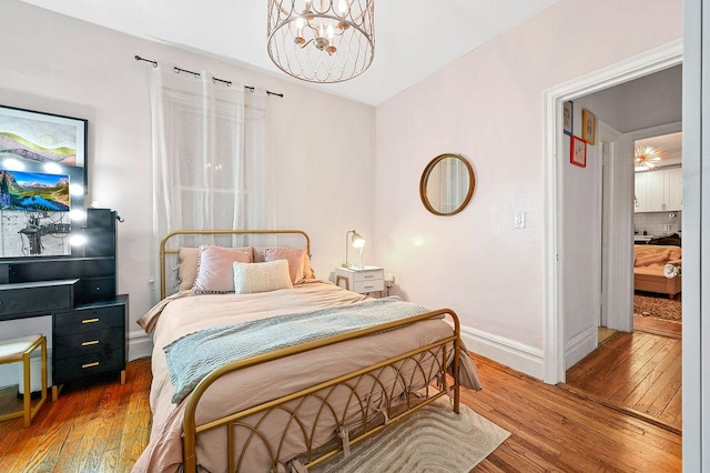 bedroom with a notable chandelier, hardwood / wood-style floors, and baseboards